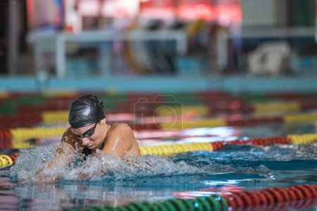Powerful and persistent professional female swimmer swimming breaststroke at speed. Endurance, effort, and focus concept.