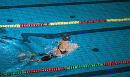 Sportlerin schwimmt im Brustschwimmen in der Schwimmbahn, streichelt, taucht ein und hebt sich zum Atmen aus dem Wasser.