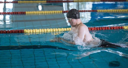 Männlicher Athlet schwimmt im Brustschwimmen im Pool, streicht, taucht ein und hebt sich zum Atmen aus dem Wasser.