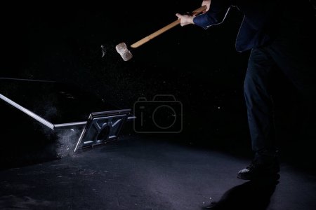 Un homme tenant un marteau de traîneau, frappant et fracassant un téléviseur plasma, isolé sur un fond noir, au ralenti verrouillé. Personnes et concepts technologiques.