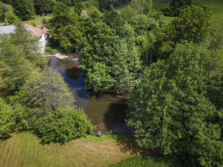 One Fishermen fishing on the river band surrounded by beautiful nature in the summer season, aerial shot. Outdoor lifestyle, relax, and unwind concepts.