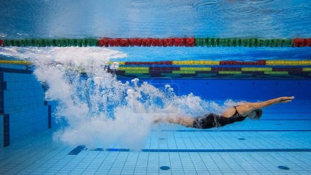 Nadadora femenina en fase de inmersión en agua, entrando y deslizándose por debajo de la superficie del agua haciendo maravillosas burbujas, tiro bajo el agua.