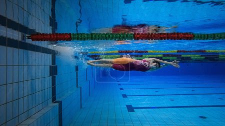 Nadadora en la fase de inmersión en agua, deslizándose por debajo de la superficie del agua, tiro bajo el agua. Concepto de deporte acuático.
