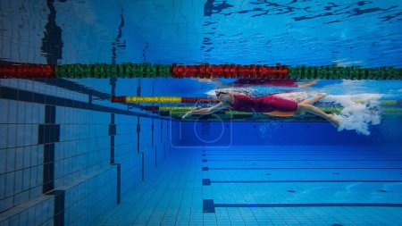 Sportlerin schwimmt im Freistil und macht einen Salto rückwärts im Becken, Unterwasserbreite.