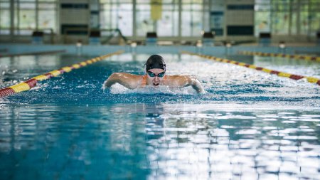 Éxito profesional nadadora nadadora mariposa accidente cerebrovascular en la piscina cubierta, vista frontal. Concepto de determinación y entrenamiento deportivo duro.