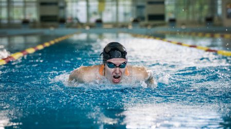 Erfolgreiche Profi-Schwimmerin schwimmt Schmetterlingsschlag im Rundenhallenbad, Vorderansicht. Konzept von Zielstrebigkeit und hartem Sporttraining.