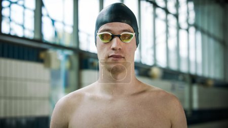 Retrato de un joven atleta profesional, nadador con gorra negra mirando a la cámara con gafas