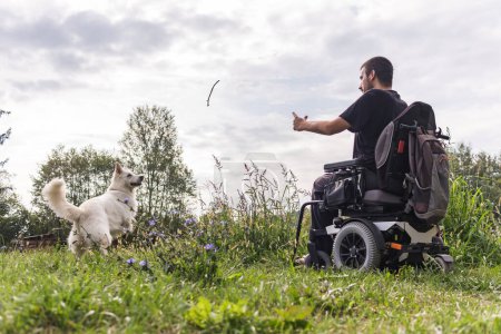 Téléchargez les photos : Homme ayant une déficience physique en fauteuil roulant et son meilleur ami un beau chien blanc, profiter d'une journée à l'extérieur. Pet love concept. - en image libre de droit