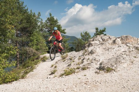 Female biker riding an electric mountain bike on a fine white stone trail, surrounded by fantastic green forest. EMTB lifestyle concept.