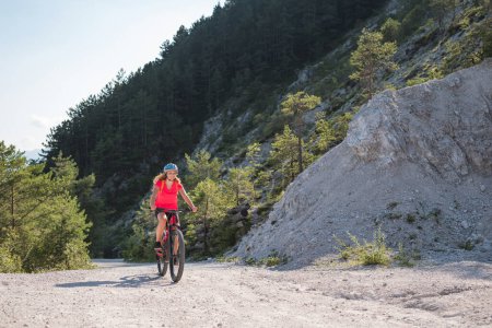 Female biker riding an electric mountain bike on a fine white stone trail, surrounded by fantastic green forest. EMTB lifestyle concept.