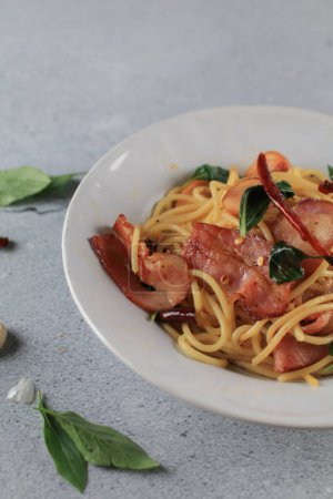 Espaguetis Bacon ají albahaca al ají en plato blanco sobre fondo gris. Menú popular plato de cocina italiana clásica. Deliciosa comida picante.