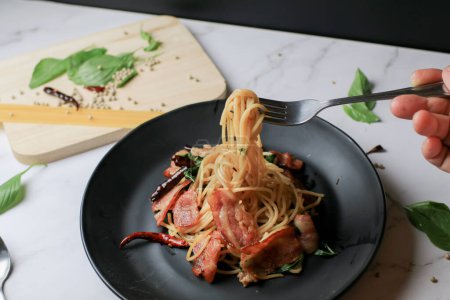 Espaguetis en tenedor con chile seco y tocino sobre mesa blanca. Menú tradicional Popular plato de cocina italiana clásica. Deliciosa comida picante.