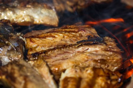 Poisson maquereau grillé avec fumée sur un barbecue au charbon de bois.