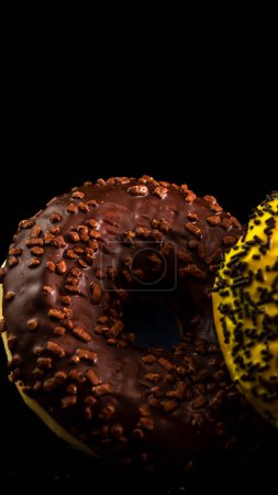 Fresh tasty colored donuts with sprinkles on black background
