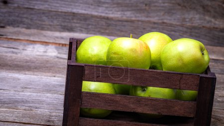 Caisse en bois avec pommes vertes mûres sur table en bois.