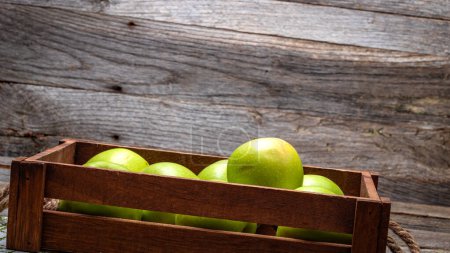 Caisse en bois avec pommes vertes mûres sur table en bois.