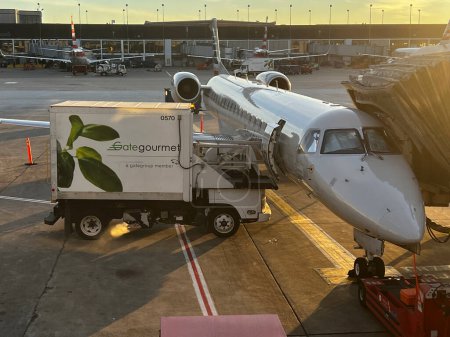 Photo for Gate Gourmet truck services an American Airlines regional jet at the gate in the morning at Chicago O'Hare International Airport. - Royalty Free Image