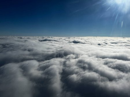 Téléchargez les photos : Vue par la fenêtre de l'avion en survolant une couche de nuages, avec un ciel bleu et un soleil éclatant. - en image libre de droit