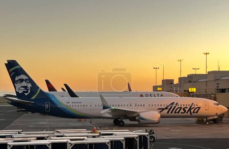 Téléchargez les photos : Les avions Alaska Airlines et Delta Airlines stationnés à la porte de l'aéroport d'Honolulu au coucher du soleil. - en image libre de droit