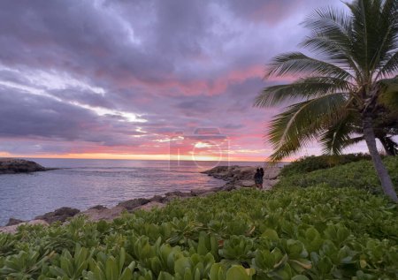 Téléchargez les photos : Mother and daughter watch a purple and pink sunset off the shore of Ko Olina Lagoons on the Hawaiian island of Oahu. - en image libre de droit