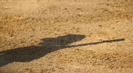Téléchargez les photos : Ombre d'un joueur de softball tenant une batte sur la terre du champ intérieur - en image libre de droit