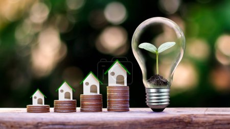 Téléchargez les photos : Model wooden house on a stack of coins and planted in a light bulb. - en image libre de droit