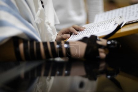 Young man practicing the reading of the Torah prior to Bar Mitzvah celebration. wearing Tefillin on the right hand.