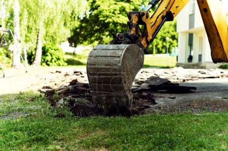 Foto de La excavadora amarilla excava asfalto con un cubo de tractor. La excavadora desmonta el asfalto en la carretera. reparaciones de carreteras - Imagen libre de derechos