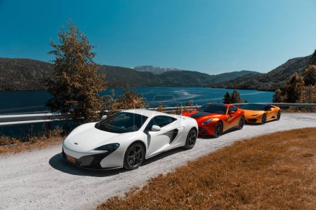 Foto de Viaje por carretera con supercoches. Mclaren 650s, Ferrari F12 y Lamborghini Huracan estacionados en una carretera de grava junto al lago. Gransherad, Noruega. 04.06.2016 - Imagen libre de derechos