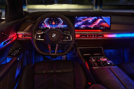 Foto de BMW Serie 7. Interior coloridamente iluminado del coche, ver centralmente en el volante desde la posición del conductor. Modelo G70, una limusina premium moderna. A la venta desde 2023. Polonia, Katowice 03.05.2023 - Imagen libre de derechos