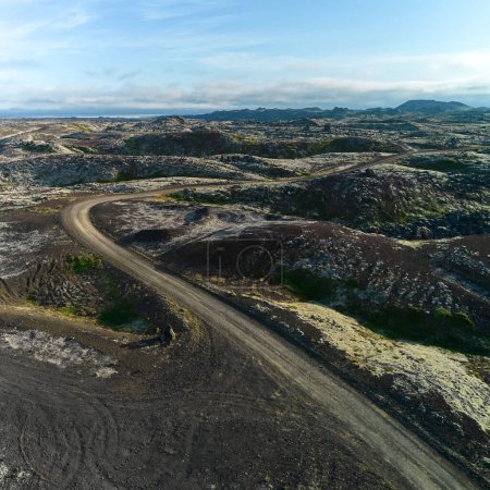 A view of the dirt road stretching to the horizon among the lava fields. Top view, photo taken from the drone. Helgafellssveit, Iceland.
