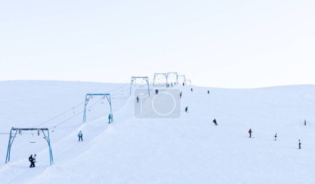 Photo for Skiing and snowboarding. A ski slope with a ski lift and small unrecognizable figures of people on a background of white snow, staffage - Royalty Free Image
