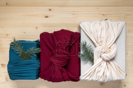 Photo for Trendy zero waste gift wrapping. Sustainable design concept. Three Christmas presents in fabric on wooden background. Flat lay - Royalty Free Image