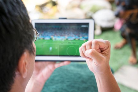 Hombre con el puño en alto, emocionado viendo los deportes de fútbol juego en la tableta digital. Concepto de estilo de vida online o digital.