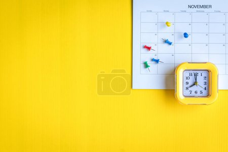 Foto de Calendario wiht pinchos de colores y reloj, vista superior. Sobre fondo amarillo, espacio de copia. - Imagen libre de derechos