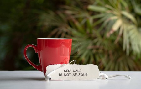 Self care is not selfish, words on white note next to coffee and earphones.