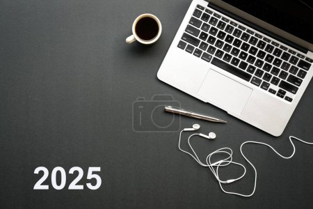 2025, texto en tapa negra con ordenador portátil, auriculares y café. Vista superior.