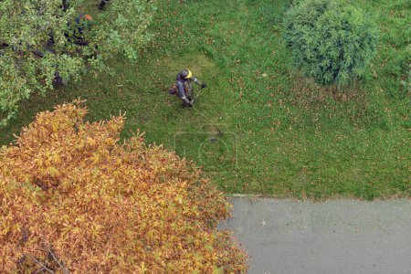Photo for Worker mows the grass with a gasoline brushcutter in the city, top view - Royalty Free Image