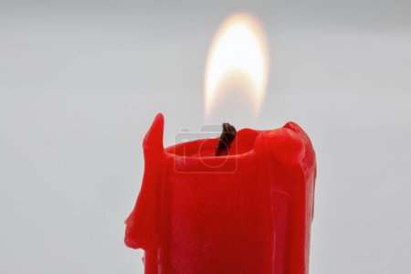 burning small red candle stub closeup on white background
