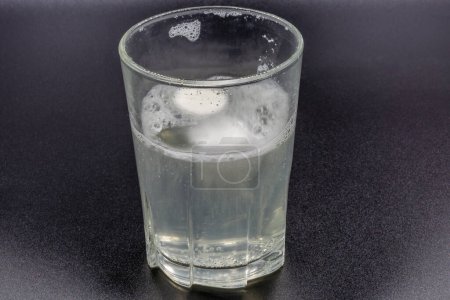 Téléchargez les photos : Comprimés effervescents instantanés dissolvants dans un verre d'eau en gros plan sur noir - en image libre de droit