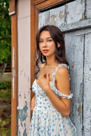 Young beautiful caucasian woman in summer dress standing against old door with cracked paint, closeup.