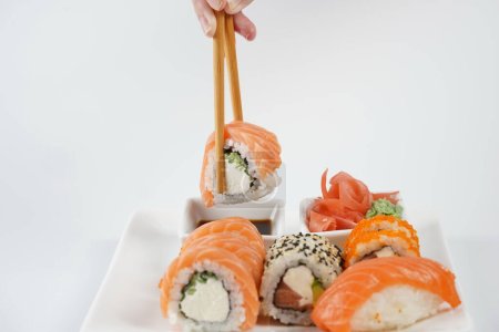 Téléchargez les photos : Sushi roll tenant dans des bâtons de nourriture. Cuisine traditionnelle japonaise - en image libre de droit