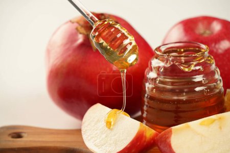 Photo for Jewish holiday Rosh Hashana celebration. Pomegranate, apples and honey traditional products for the holyday. Pouring honey on apple and pomegranate - Royalty Free Image