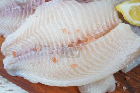 Fresh tilapia fish fillet sliced for steak or salad with herbs spices and lemon