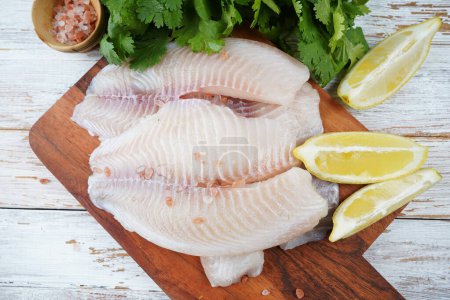 Fresh tilapia fish fillet sliced for steak or salad with herbs spices and lemon