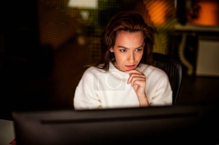 Foto de Fotografía de una mujer de negocios seria y reflexiva sentada en la mesa con computadora en la oficina al final de la noche. - Imagen libre de derechos