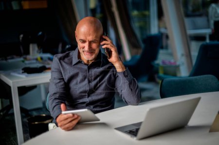 Téléchargez les photos : Businessman using digital tablet and making a call while sitting in a modern office. Multitasking. - en image libre de droit