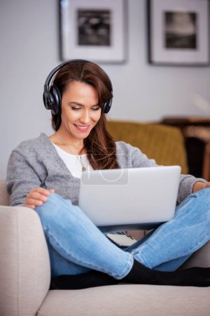 Photo for Full length of beautiful middle aged woman with headphones using a laptop while browsing on the internet. - Royalty Free Image