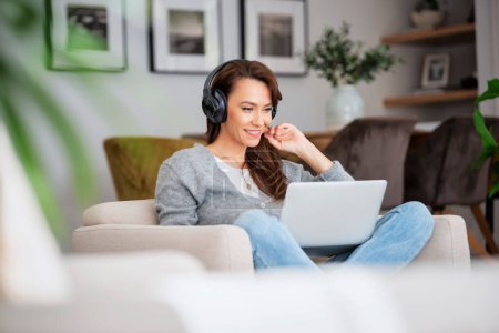 Photo for Close-up of beautiful middle aged woman with headphones using a laptop while browsing on the internet. - Royalty Free Image
