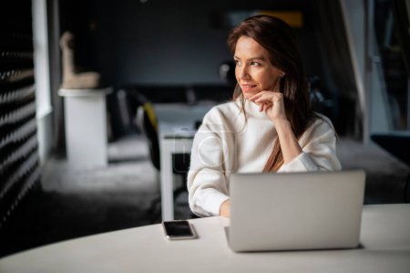 Foto de Mujer de mediana edad de negocios utilizando el ordenador portátil mientras está sentado en el escritorio en la oficina. Ejecutiva mujer de negocios vistiendo suéter. - Imagen libre de derechos